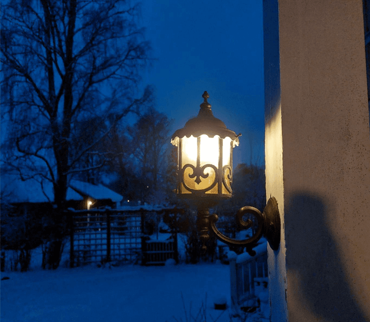 Upplyst lykta på en husvägg en vinterkväll